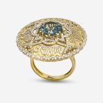An opulent ring featuring 18-karat gold and intricate diamond details, with a large blue stone (topaz) at its center, adorned with cage and calligraphy motifs.