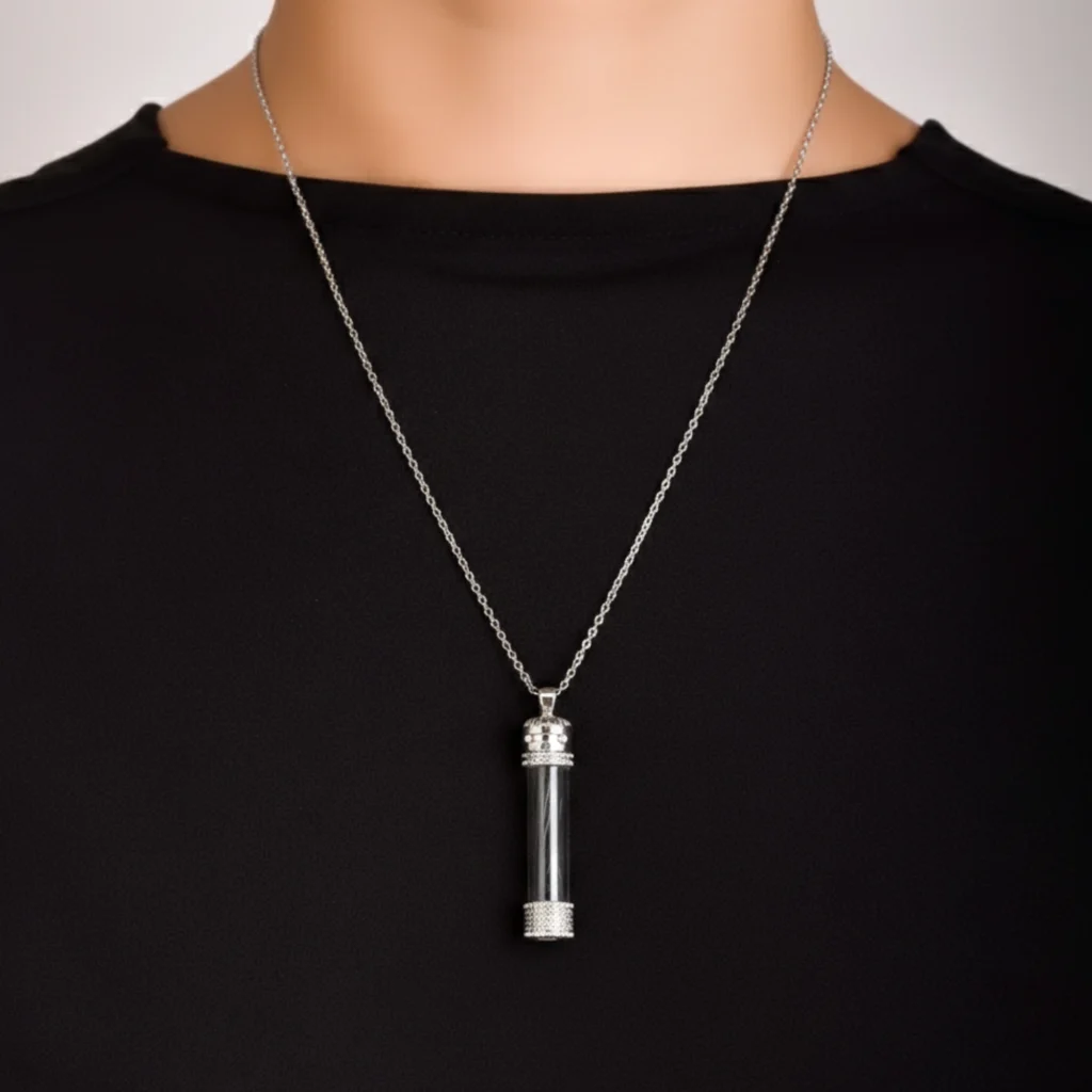 An aesthetic silver necklace made of 925 sterling silver, inspired by the cylindrical form of the historical Sakal-ı Şerif cases, with the original black Kaaba cover fabric visible inside its transparent case.